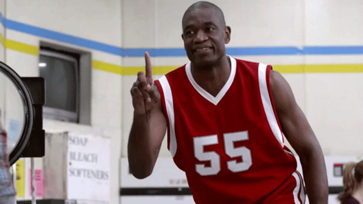 Basketball player Dikembe Mutumbo grinning and waving his finger in denial.